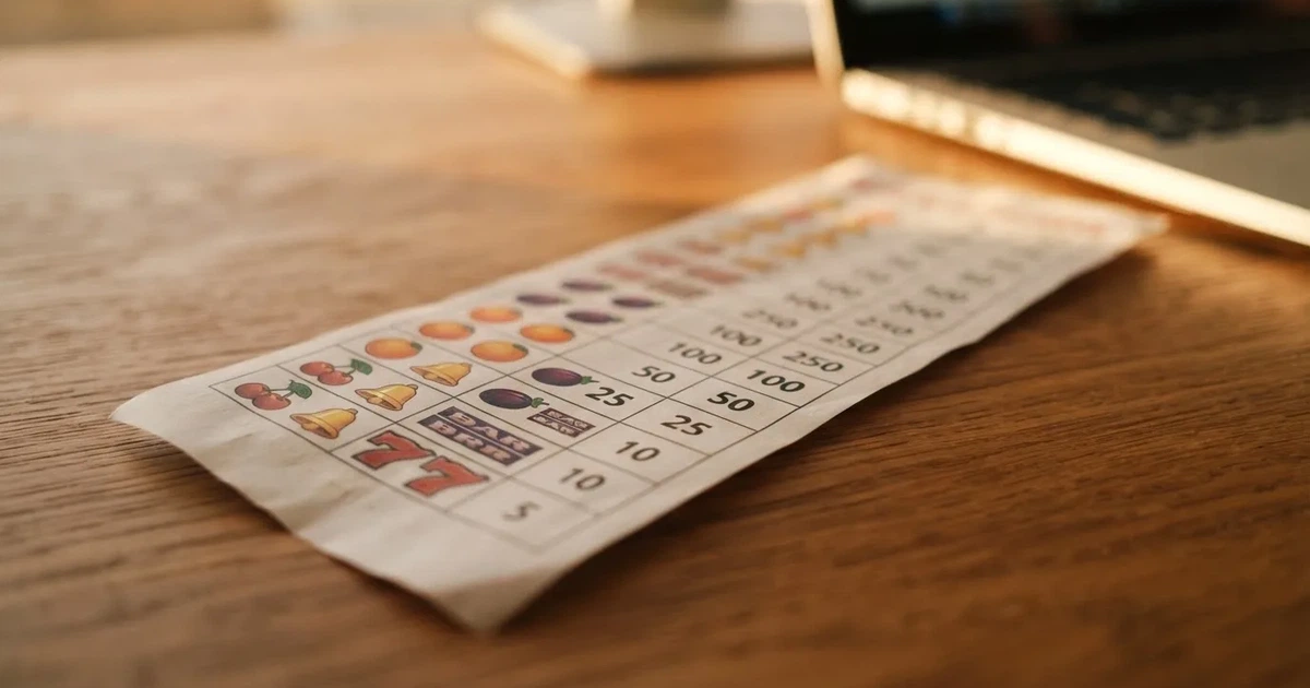 A printed strip of generic slot symbols and payout numbers laid on a desk, like a reference chart rather than a live game.